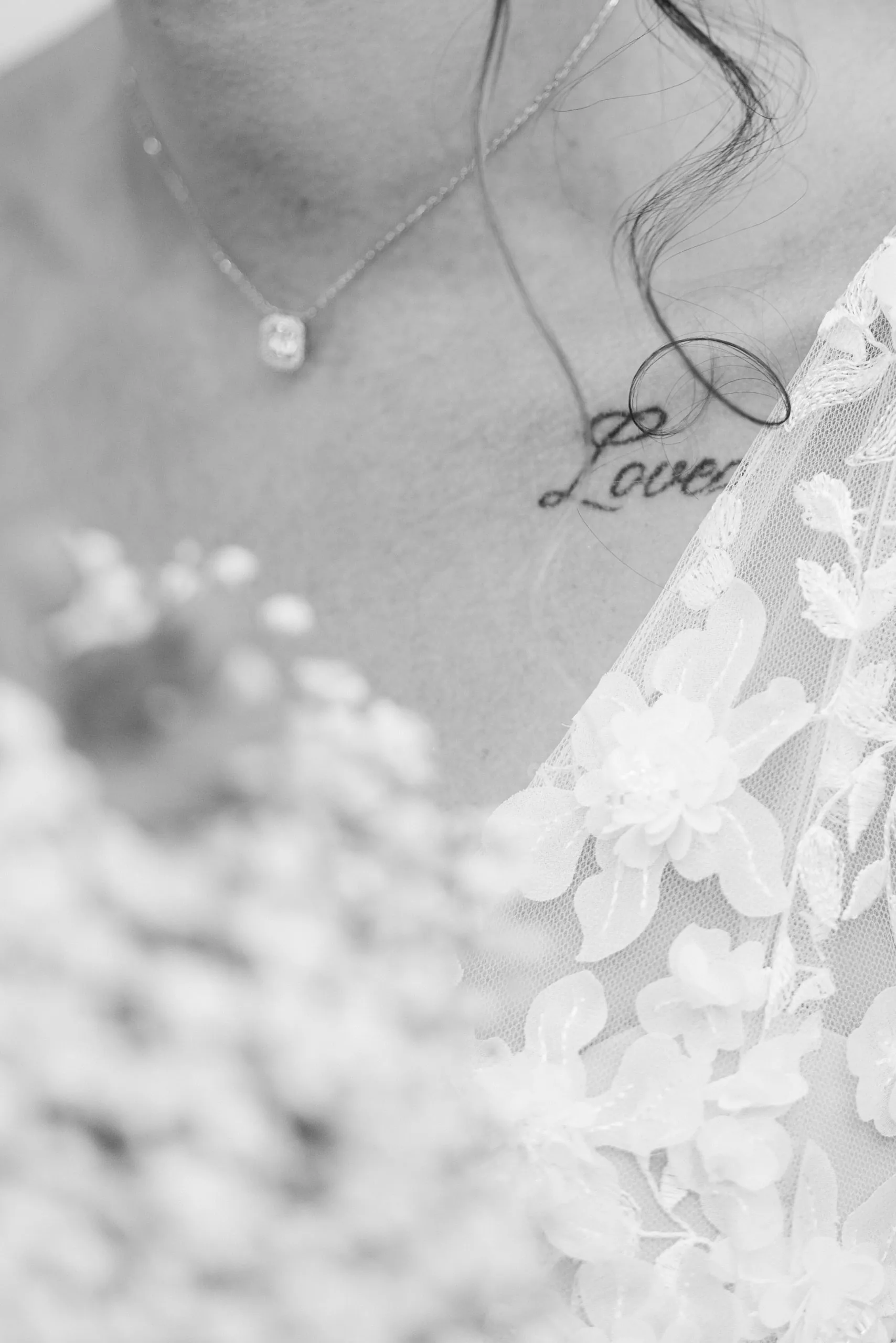 Gros plan noir et blanc sur le collier de la mariée et son tatouage
