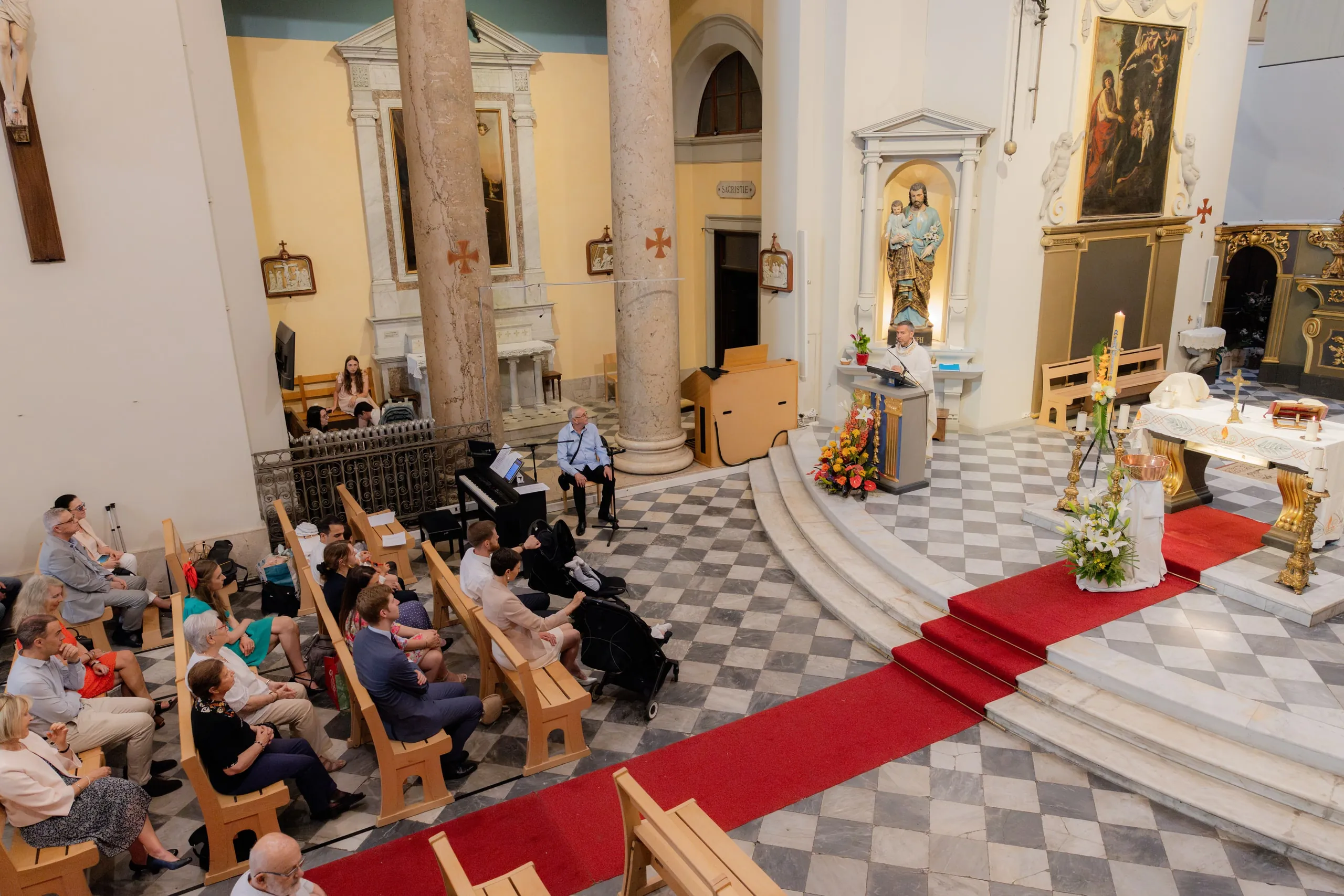 La nef de l'église vue d'en haut : les proches assis sur les bancs, le tapis rouge menant à l'autel