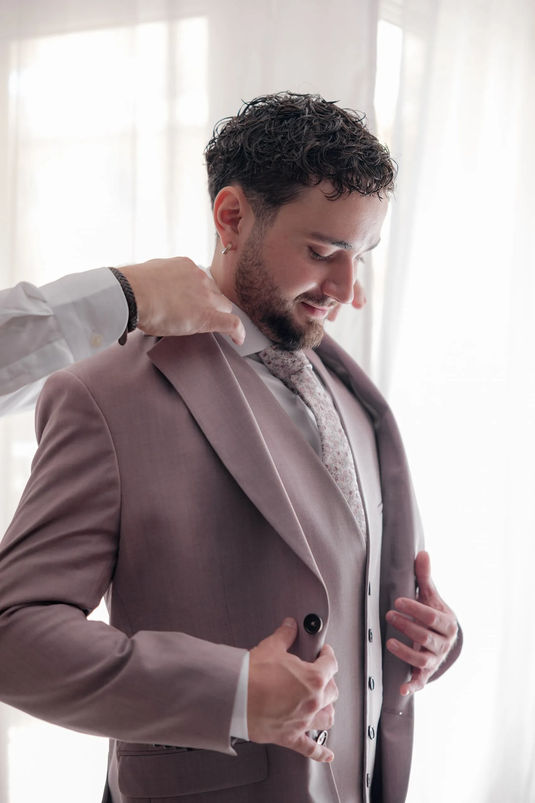 Hugo boutonne sa veste mauve devant la fenêtre