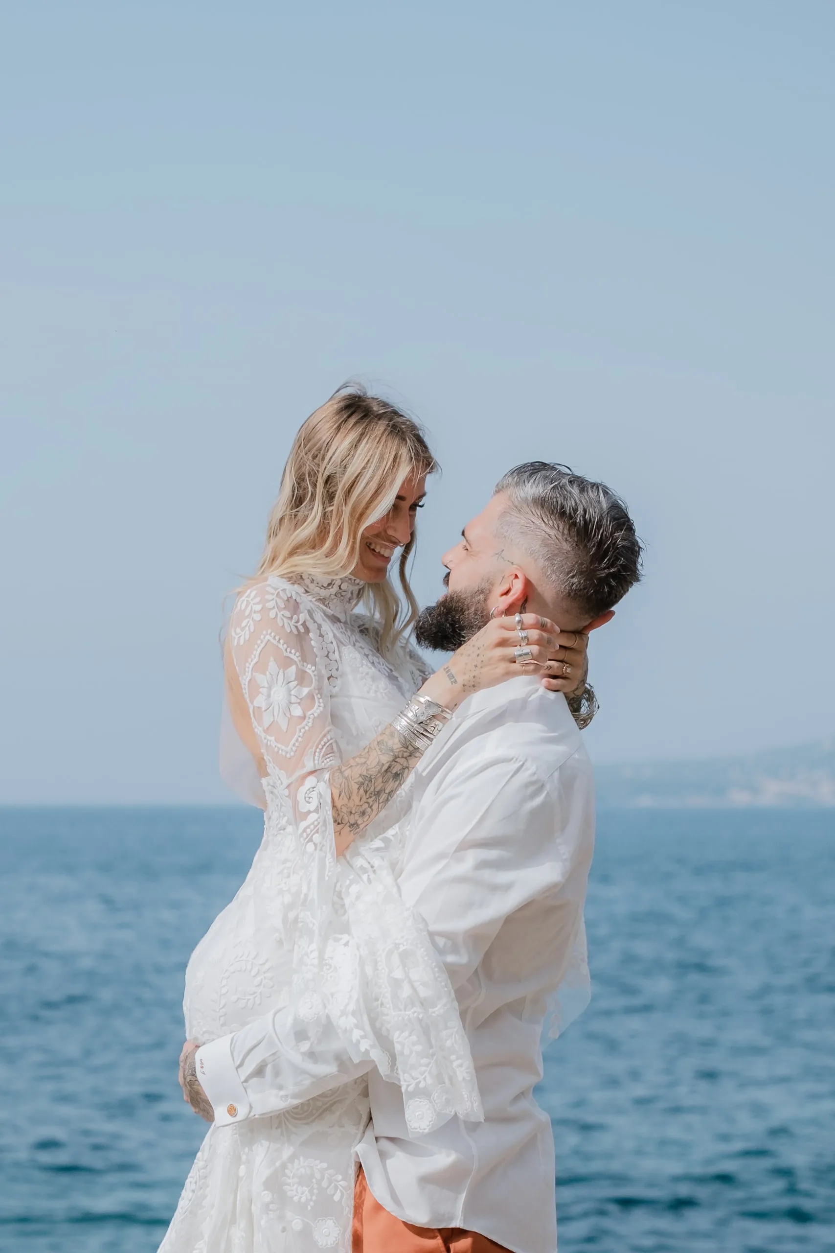 La mariée pose ses mains sur le visage du marié, la mer derrière eux