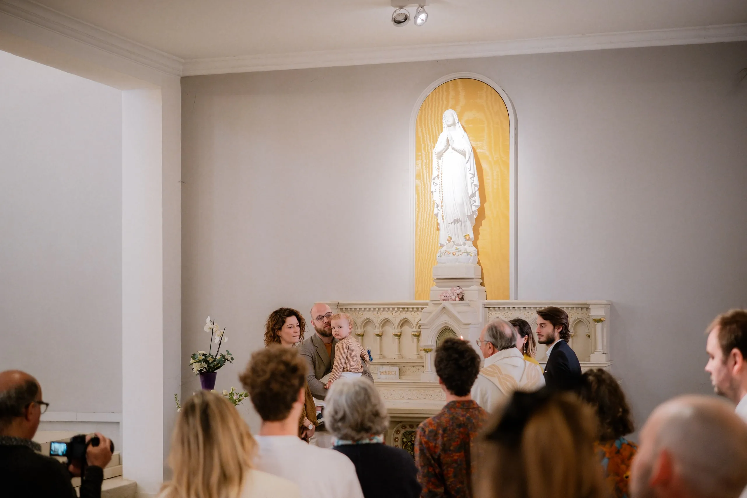 Les invités, vus de dos, face à la famille réunie devant la statue de la Vierge
