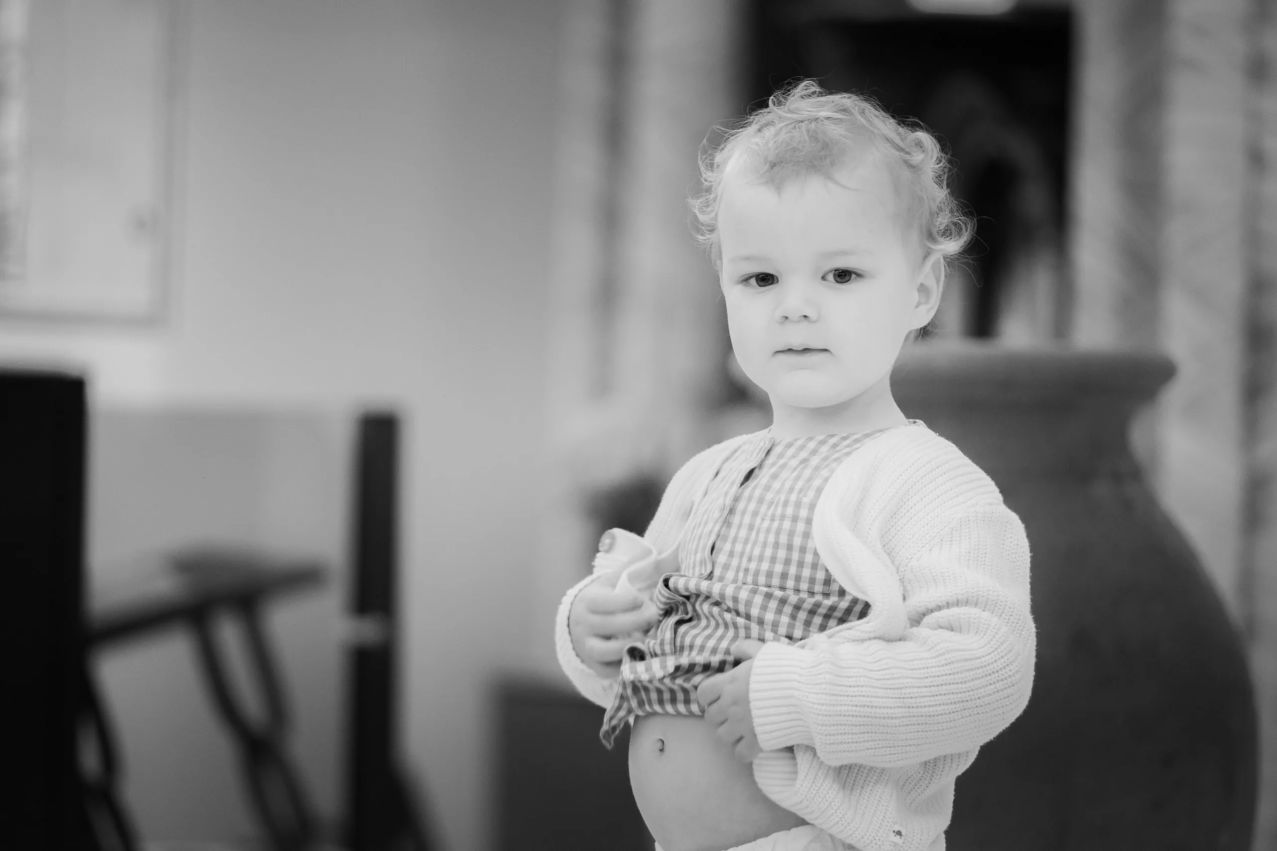 Portrait en noir et blanc d'un petit garçon aux cheveux bouclés, debout à côté d'une grande jarre