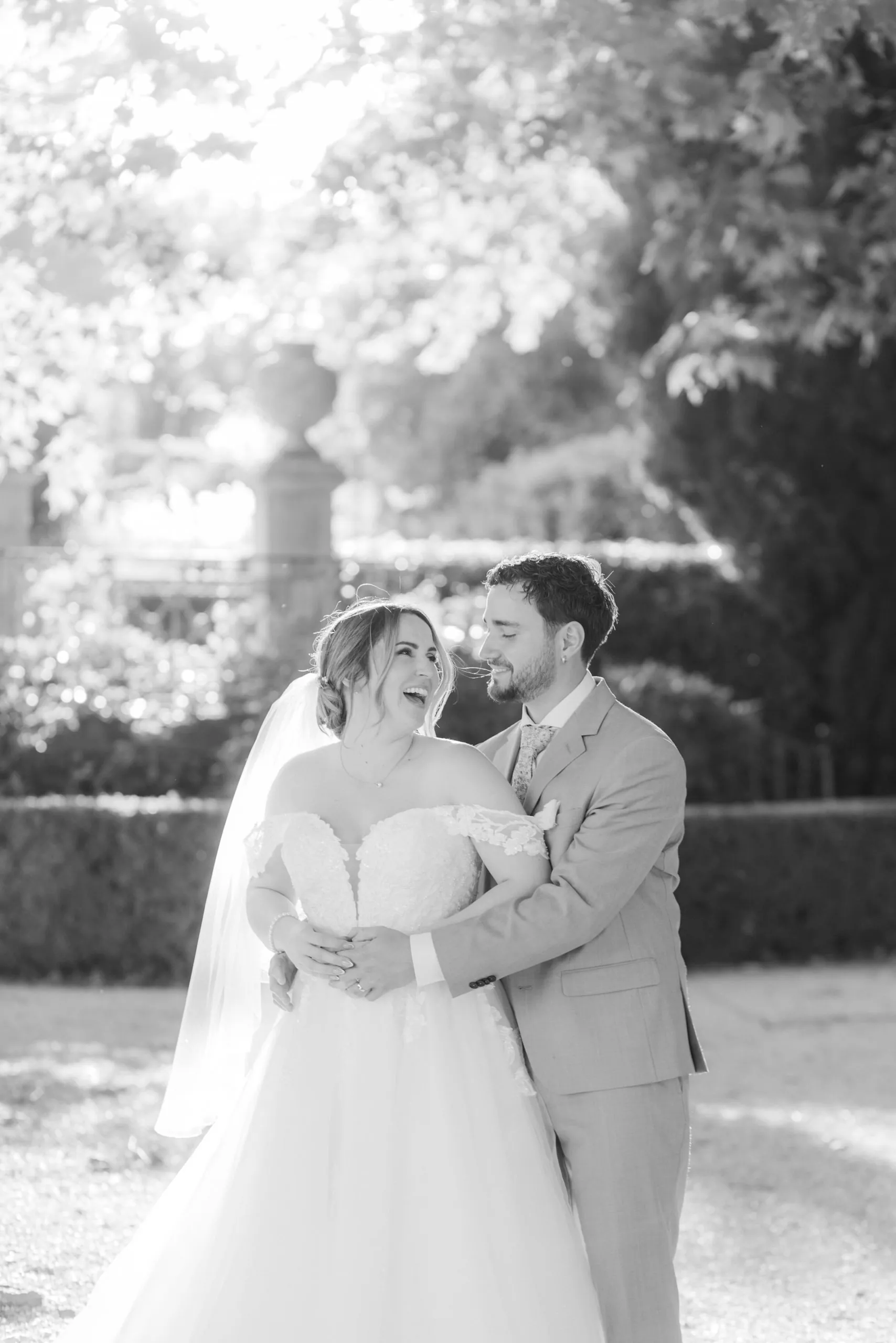 Les mariés enlacés dans le parc, la mariée rit aux éclats, en noir et blanc