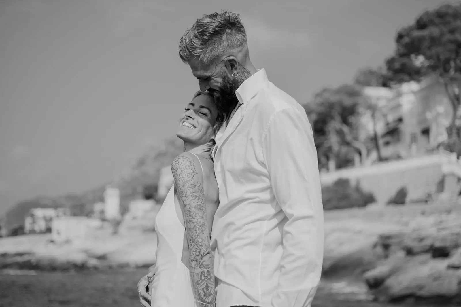 Les mariés enlacés au bord de la mer, la mariée sourit, les yeux fermés, en noir et blanc